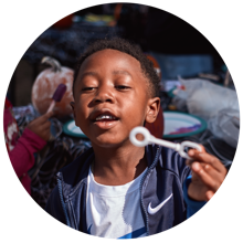 A young child smiling while blowing bubbles.