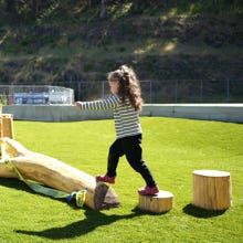 A child with their arms out-stretched balancing on wooden playground equipment.