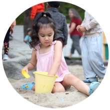 A young child playing with a bucket in a sand pit at a playground.