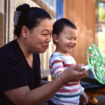 A toddler and her mother smile while playing with bubbles.