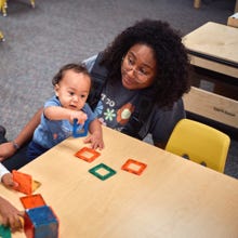 A caregiver watching a toddler play with tiles.